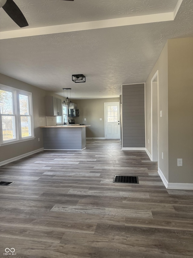 unfurnished living room with visible vents, baseboards, a textured ceiling, and dark wood-style flooring