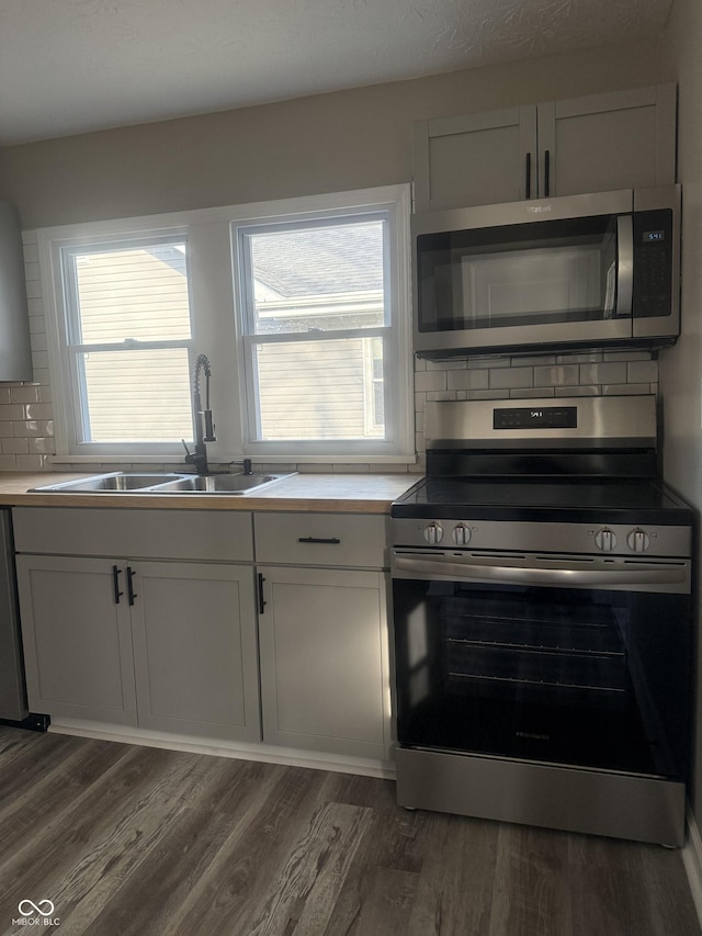 kitchen with a sink, decorative backsplash, appliances with stainless steel finishes, and dark wood-style floors