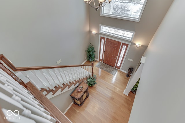 entryway with light wood-type flooring, a notable chandelier, baseboards, a towering ceiling, and stairs