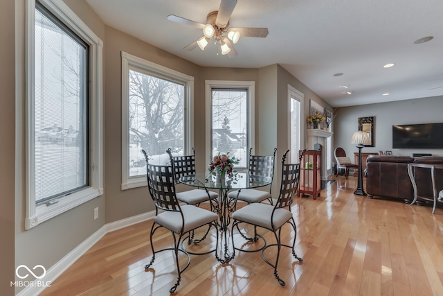 dining room featuring baseboards, ceiling fan, recessed lighting, light wood-style flooring, and a fireplace