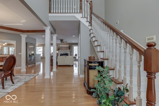 entryway with a ceiling fan, decorative columns, a fireplace, stairs, and light wood-style floors