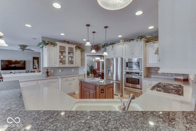 kitchen featuring glass insert cabinets, recessed lighting, appliances with stainless steel finishes, stone countertops, and a sink