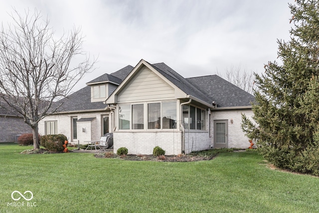 view of front facade with brick siding, roof with shingles, a front lawn, and a sunroom