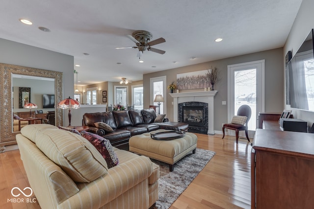 living area with baseboards, a premium fireplace, light wood-style flooring, recessed lighting, and ceiling fan