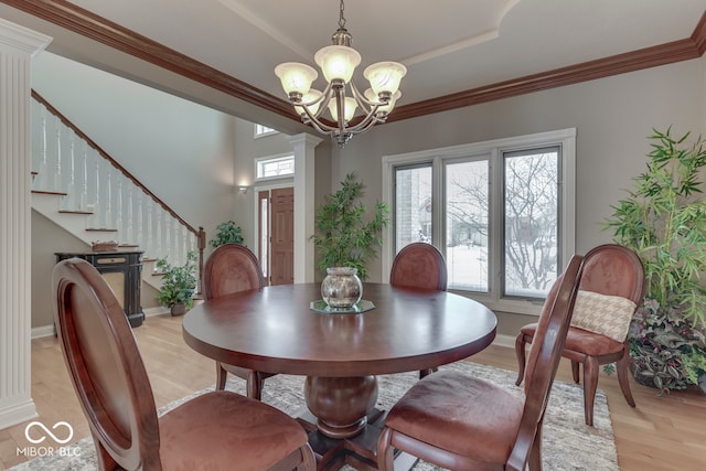 dining room with stairs, light wood-type flooring, ornamental molding, decorative columns, and an inviting chandelier