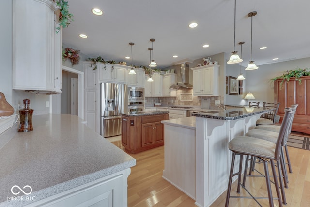 kitchen featuring stone counters, light wood finished floors, appliances with stainless steel finishes, and wall chimney range hood