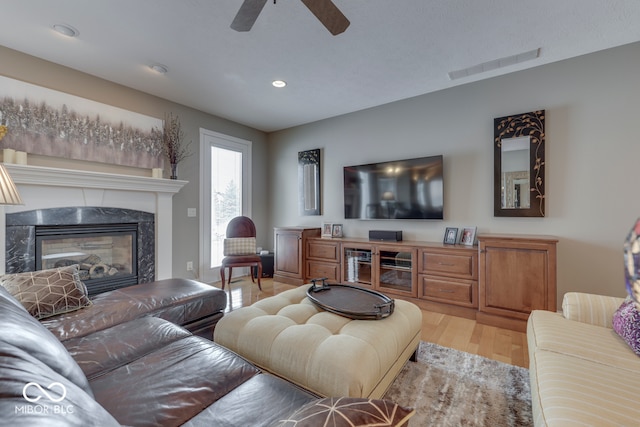 living area featuring a ceiling fan, wood finished floors, visible vents, a premium fireplace, and recessed lighting