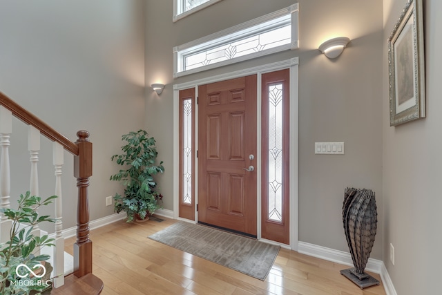 foyer featuring light wood-style flooring, baseboards, and a towering ceiling