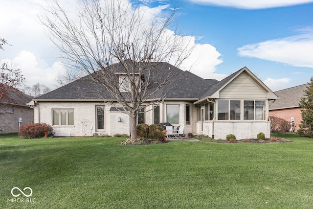 view of front of property with a front lawn, brick siding, a sunroom, and a shingled roof