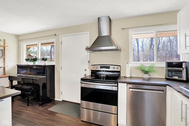 kitchen featuring dark countertops, appliances with stainless steel finishes, white cabinetry, and wall chimney range hood