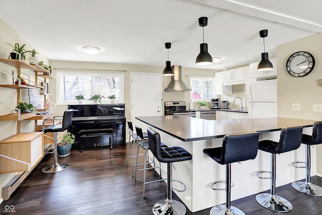 kitchen with dark countertops, appliances with stainless steel finishes, dark wood-style floors, and wall chimney range hood