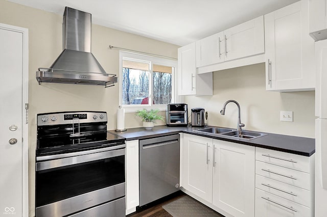 kitchen featuring dark countertops, wall chimney range hood, white cabinets, stainless steel appliances, and a sink