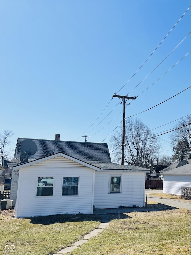 exterior space with a yard, fence, roof with shingles, and a chimney