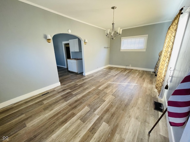 unfurnished dining area featuring visible vents, crown molding, baseboards, wood finished floors, and arched walkways