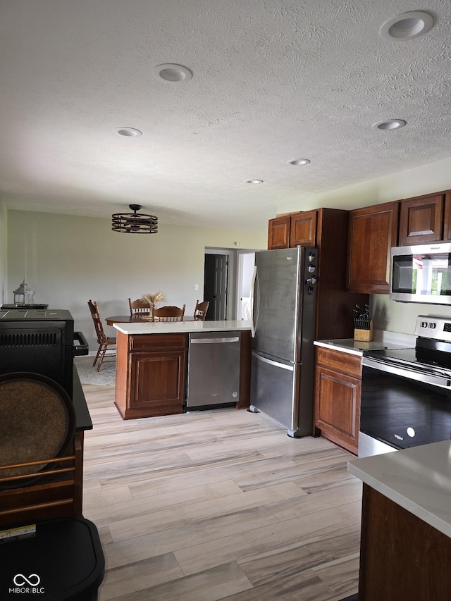 kitchen featuring light wood finished floors, appliances with stainless steel finishes, light countertops, and a peninsula