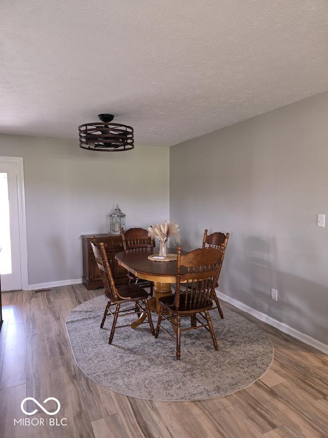 dining space with baseboards, a textured ceiling, and wood finished floors