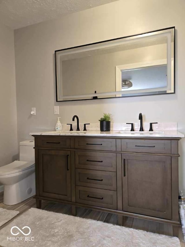 bathroom with double vanity, a textured ceiling, toilet, and a sink