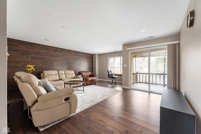 living area with baseboards, visible vents, dark wood-type flooring, wood walls, and an accent wall