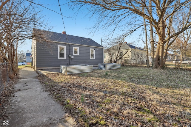 back of property featuring a vegetable garden, a shingled roof, a chimney, and fence