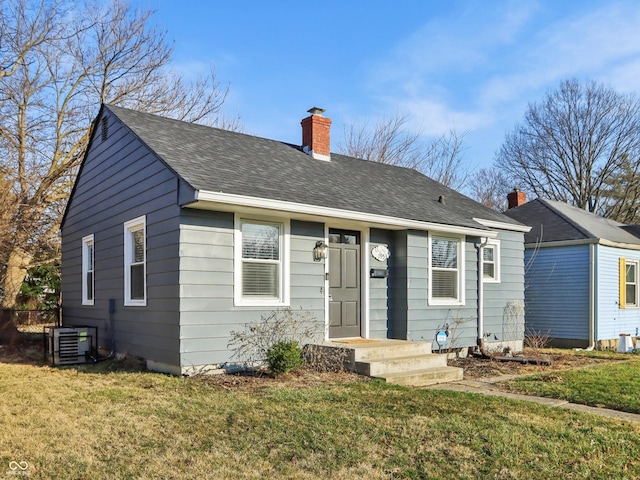 bungalow-style house featuring roof with shingles, a chimney, central AC, and a front lawn