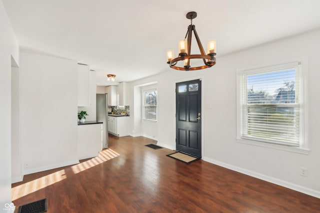 foyer entrance featuring an inviting chandelier, baseboards, visible vents, and dark wood-type flooring