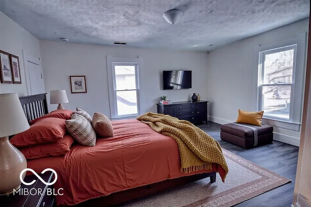 bedroom with visible vents, a textured ceiling, baseboards, and wood finished floors