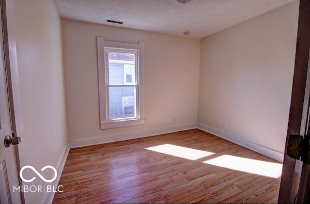 empty room featuring visible vents, baseboards, and wood finished floors