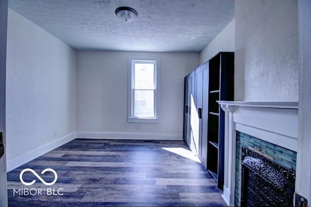 unfurnished living room featuring a fireplace, a textured ceiling, baseboards, and wood finished floors