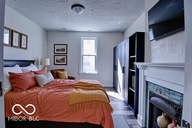 bedroom with a fireplace with flush hearth, baseboards, visible vents, and wood finished floors