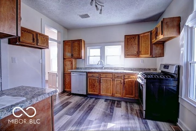 kitchen with dishwashing machine, brown cabinetry, gas stove, visible vents, and a sink