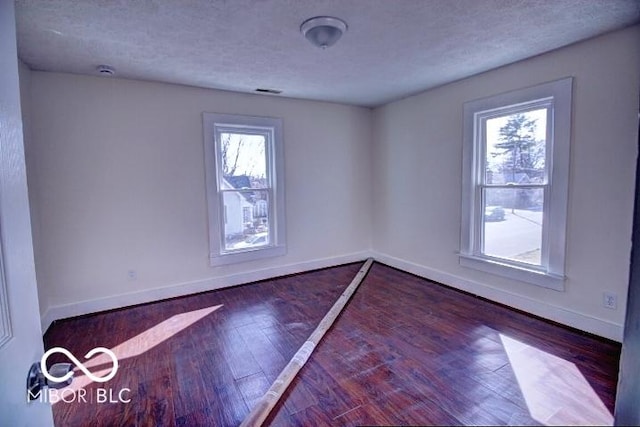 empty room featuring baseboards, wood-type flooring, and a textured ceiling