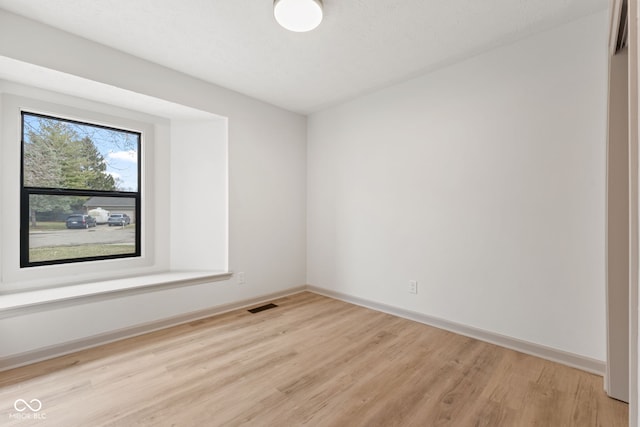 empty room with light wood-style flooring, baseboards, and visible vents