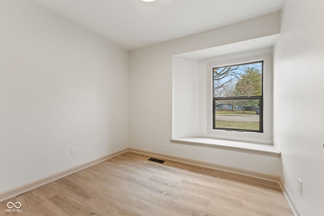 spare room featuring light wood-style floors, visible vents, and baseboards