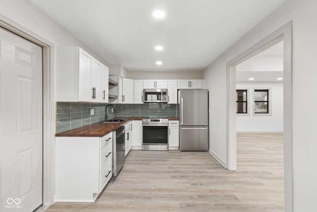 kitchen with a sink, backsplash, white cabinets, stainless steel appliances, and open shelves