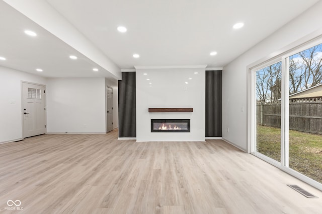 unfurnished living room featuring visible vents, recessed lighting, light wood-style flooring, and a glass covered fireplace