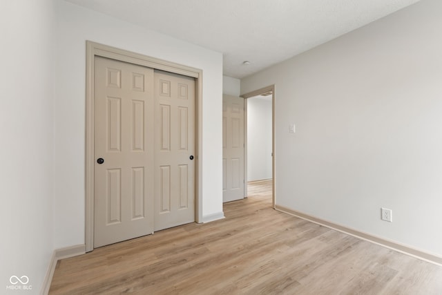 unfurnished bedroom featuring a closet, baseboards, and light wood-style floors