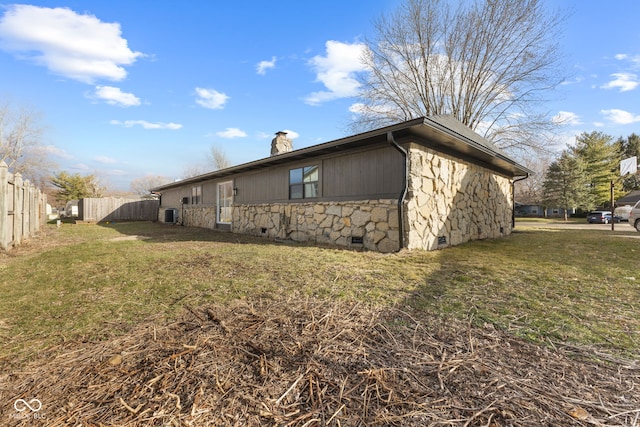 view of side of home with stone siding, fence, a yard, crawl space, and a chimney