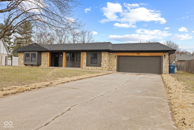 view of front facade with a shingled roof, fence, concrete driveway, a garage, and stone siding