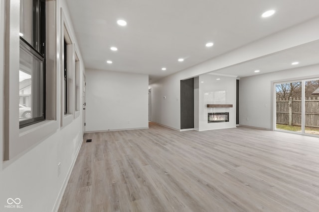 unfurnished living room with recessed lighting, light wood-style flooring, and a glass covered fireplace