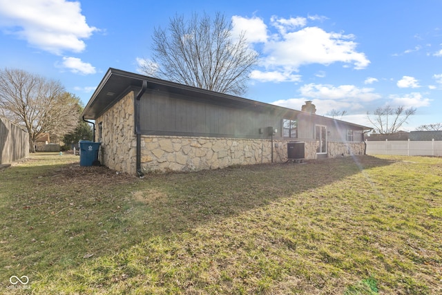 view of side of property with fence, a yard, a chimney, stone siding, and central air condition unit