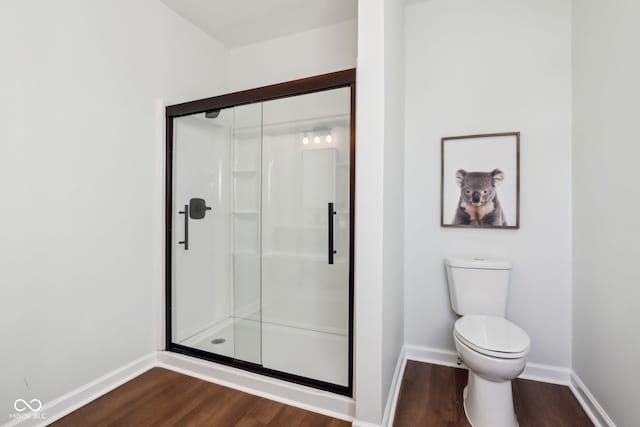 bathroom featuring toilet, wood finished floors, a stall shower, and baseboards