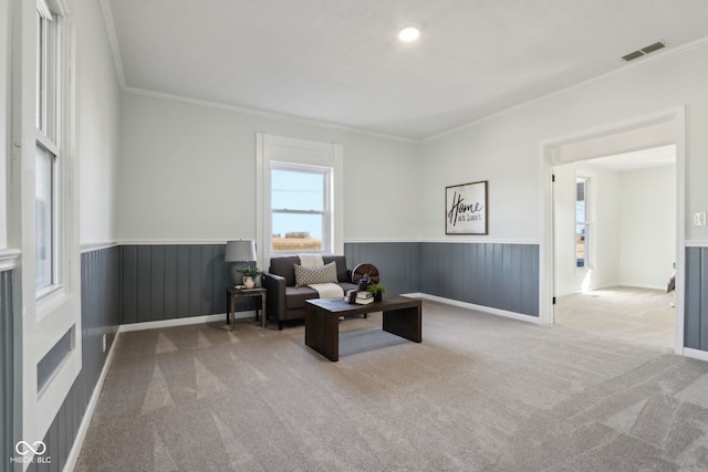 living area featuring a wainscoted wall, visible vents, carpet flooring, and crown molding