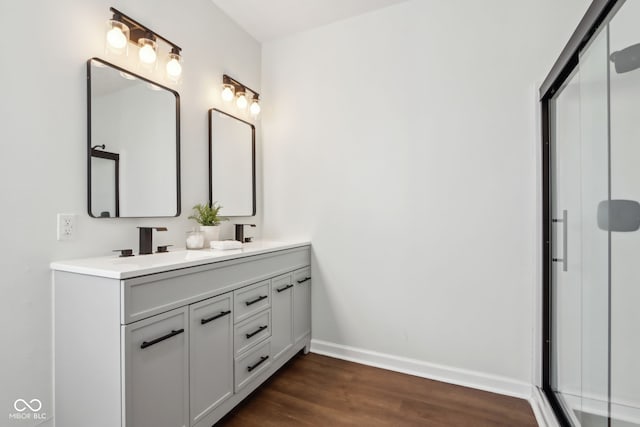 full bathroom with a shower with shower door, a sink, wood finished floors, double vanity, and baseboards