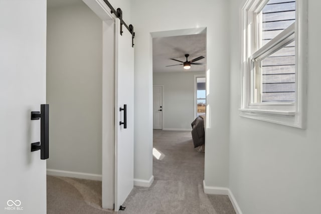 hallway with a barn door, carpet, and baseboards