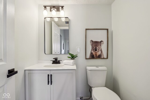 half bath featuring toilet, vanity, and a textured ceiling