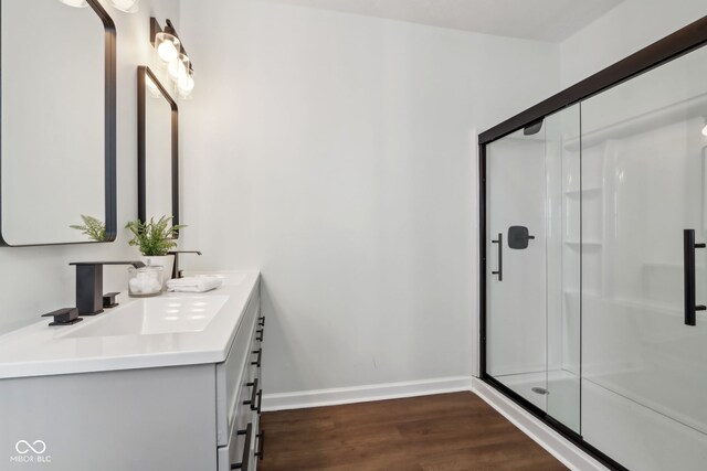 bathroom with a shower stall, baseboards, double vanity, wood finished floors, and a sink