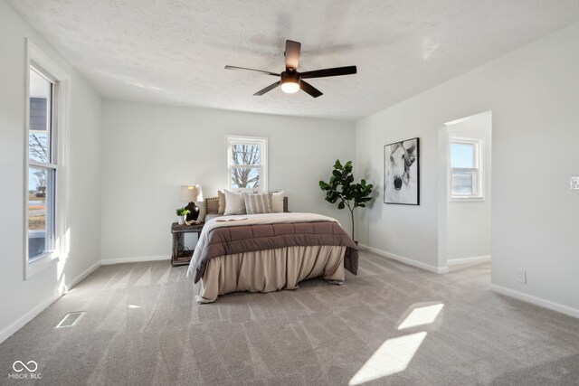 carpeted bedroom with visible vents, baseboards, a textured ceiling, and a ceiling fan