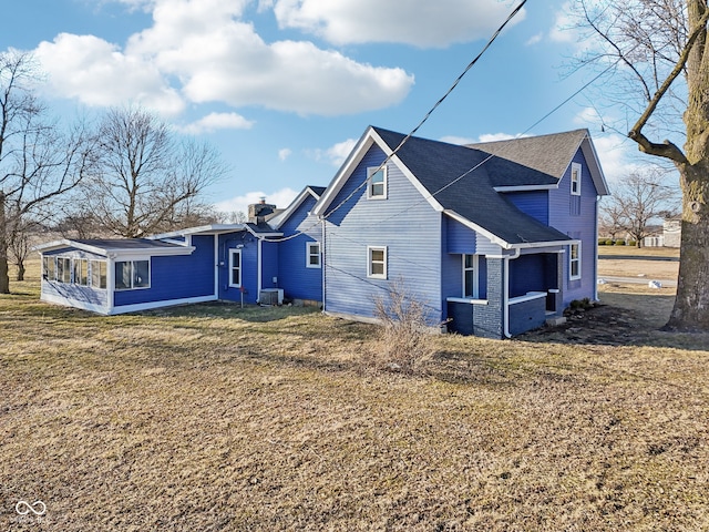 back of property featuring brick siding, central AC, roof with shingles, a lawn, and a sunroom