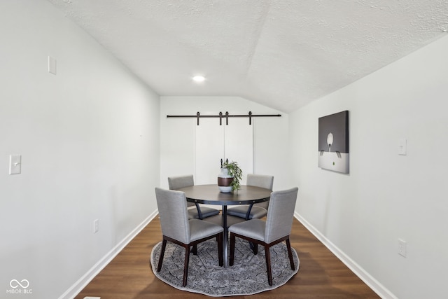 dining space featuring baseboards, a textured ceiling, dark wood-type flooring, and a barn door