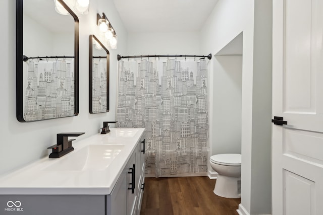 full bath featuring toilet, a shower with shower curtain, double vanity, wood finished floors, and a sink